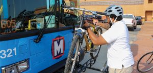 Bring your bike on MetroBus step 2: Man lifting up a bike to place the tires into the bike rack slots.